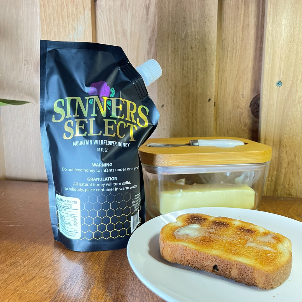 Sinners Select honey sitting on counter with toast on a plate and butter in a butter dish