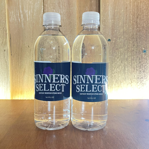 Two bottles of Sinner's Select water on a wooden surface.